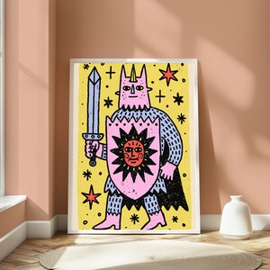 May include: A framed art print featuring a stylised pink horned figure holding a grey sword and a pink shield with a black sun graphic. The background is yellow with black stars and crosses. The figure wears pink boots and a black cape.