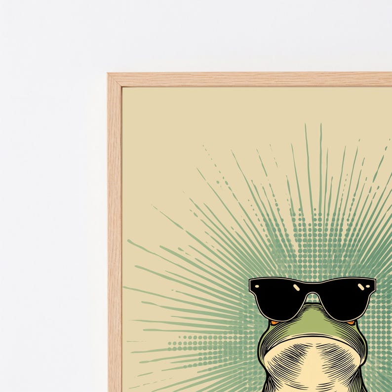 May include: A framed wall art print featuring a green frog wearing black sunglasses. The frog is centered against a light beige background with a radiating green sunburst pattern composed of lines and dots emanating from behind the frog's head.