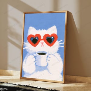 May include: A framed art print featuring a fluffy white cat against a solid light blue background. The cat wears large red heart-shaped sunglasses and holds a small white mug filled with dark coffee, rendered in a soft, textured illustration style.