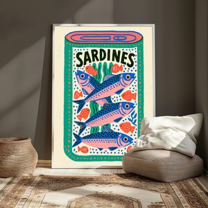 May include: A rectangular wall art print featuring a stylized illustration of a sardine tin. The design includes three large blue and pink fish, several smaller orange fish, and green seaweed accents on a cream background with the word SARDINES.