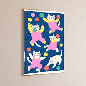 K&ouml;nnte beinhalten: Ein gerahmter Wandkunstdruck mit einem dunkelblauen, texturierten Hintergrund und f&uuml;nf wei&szlig;en Katzen in rosa Latzhosen. Die Katzen sind in verschiedenen verspielten Posen dargestellt und interagieren mit gelben, orangen und gr&uuml;nen Kreisen.