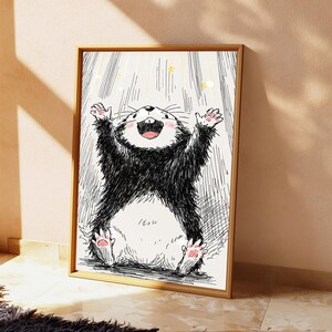 May include: A framed wall art print featuring a black and white ink-style illustration of a cheerful, furry creature with its arms raised upward. The creature has a white belly, pink paw pads, and a wide, happy expression with visible teeth.