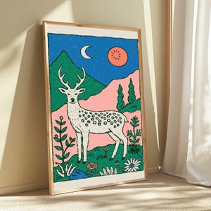 May include: A framed art print featuring a white spotted deer standing in a landscape with green mountains, pink hills, and a blue sky. The scene includes a white crescent moon, a round orange sun, and various stylized flowers in the foreground.