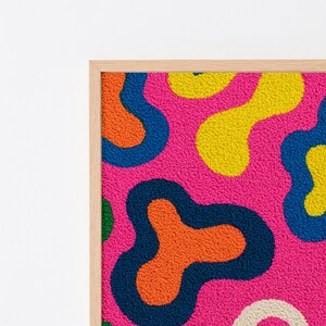 May include: A rectangular wall art piece featuring a tufted, textured surface with an abstract pattern of organic, amoeba-like shapes in vibrant shades of hot pink, bright yellow, orange, deep blue, and green, framed in a light-toned wood.