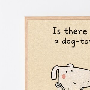 K&ouml;nnte beinhalten: Ein gerahmter Kunstdruck auf strukturiertem cremefarbenem Papier mit einer schwarzen Strichzeichnung eines Hundes mit rosa Wange. Der Text lautet: Is there a dog-toy. Der Rahmen besteht aus hellem Holz mit sichtbarer Maserung.