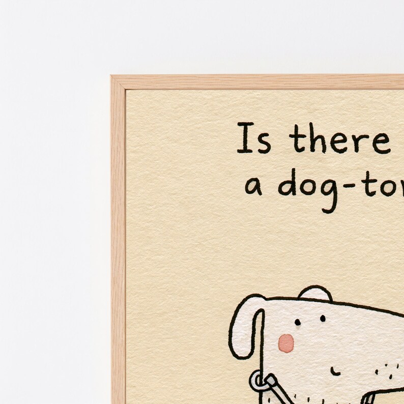 K&ouml;nnte beinhalten: Ein gerahmter Kunstdruck auf strukturiertem cremefarbenem Papier mit einer schwarzen Strichzeichnung eines Hundes mit rosa Wange. Der Text lautet: Is there a dog-toy. Der Rahmen besteht aus hellem Holz mit sichtbarer Maserung.