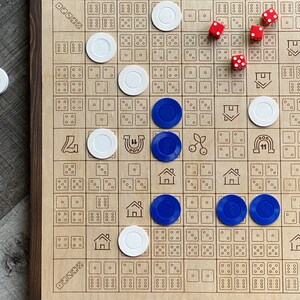 May include: A wooden board game with a dark brown frame. The game board has a grid pattern with various symbols and dice patterns. White and blue game pieces are scattered across the board, along with red dice.