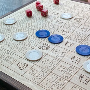 May include: A wooden board game with a dark brown frame. The light-colored game board features etched squares with dice patterns and symbols. Red dice and blue and white game chips are scattered across the board. A fun game for family and friends.