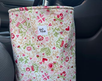 Puede incluir: Un contenedor cilíndrico de tela con fondo crema y un patrón repetitivo de corazones rojos, flores rosas y enredaderas verdes. Una etiqueta rectangular blanca con el texto negro "Rafi Made" está cosida en la parte central delantera.