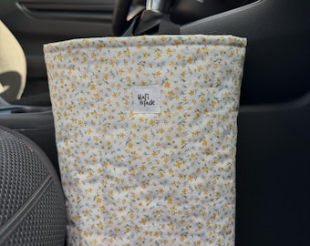 May include: A rectangular fabric car trash bag featuring a white background with a small yellow and green floral pattern. A white square fabric label is centered on the front with the black text "Rafi Made" printed in a stylized font.