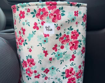 Puede incluir: Un contenedor de tela cilíndrico con fondo blanco y un patrón floral repetitivo en tonos rosa brillante, rosa oscuro y turquesa claro. Una pequeña etiqueta rectangular blanca con el texto negro "Rafi Made" está cosida en la parte frontal.