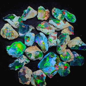 Peut inclure: Une collection de pierres d'opale brutes aux couleurs vives. Les opales présentent un mélange de bleus, de verts, de rouges et de jaunes, avec un jeu de couleurs sur leurs surfaces. Les pierres sont posées sur un fond noir.