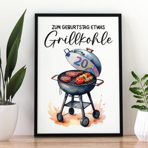 Könnte beinhalten: Ein schwarzer gerahmter Druck mit einer Aquarell-Illustration eines Grills mit einem Zwanzig-Euro-Schein darauf. Der Grill ist gefüllt mit Fleisch und Gemüse. Der Text "Zum Geburtstag etwas Grillkohle" steht in Schwarz oben auf dem Druck.