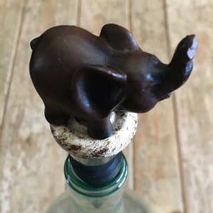 May include: A brown ceramic elephant bottle stopper with a white base. The elephant's trunk is raised and its ears are large.