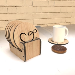 Puede incluir: Un juego de seis posavasos de madera con un diseño de corazón, apilados en un soporte de madera. Los posavasos son de madera marrón claro y tienen un diseño de corazón marrón oscuro. El soporte también es de madera marrón claro y tiene un diseño de corazón marrón oscuro.