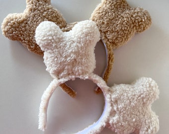 Pode incluir: Duas orelhas de faixa de cabeça peludas, duas brancas e duas marrons. As orelhas de faixa de cabeça têm a forma de orelhas de urso. As faixas de cabeça são brancas.