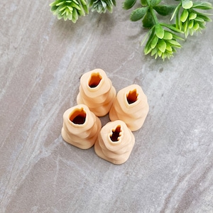 May include: Four beige plastic cookie cutters with different leaf shapes. The cutters are stacked on top of each other.
