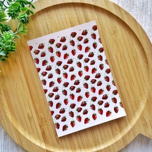 May include: A sheet of white paper with a repeating pattern of red strawberries. The strawberries are drawn in a simple, watercolour style.