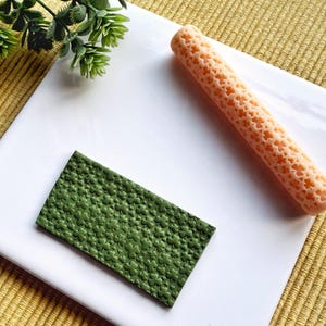 May include: A green textured rolling pin and a peach-coloured rolling pin with a honeycomb pattern.
