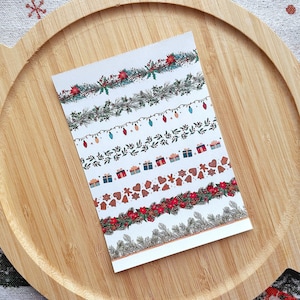 Op de afbeelding: Een vel wit papier met verschillende kerstthema-randen erop gedrukt. De randen omvatten kransen, lichten, cadeaus, peperkoek en hulst.
