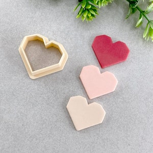Könnte beinhalten: Drei herzförmige Ausstecher, einer aus Plastik und zwei aus Fondant. Der Plastik-Ausstecher ist beige und die Fondant-Ausstecher sind rosa und beige.
