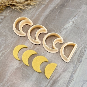 Op de afbeelding: Set van zes plastic koekjesvormen in de vorm van halve manen. De vormen zijn in een rij gerangschikt, met de grootste vorm links en de kleinste vorm rechts. De vormen zijn lichtbeige.