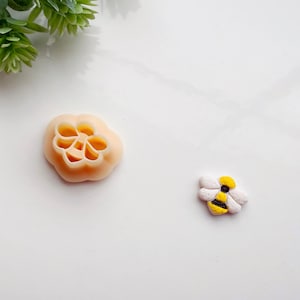 May include: Two silicone molds for baking, one shaped like a flower and the other shaped like a bee. The bee mold is yellow and black.