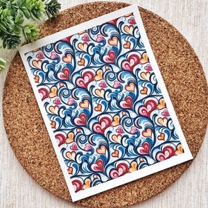 May include: A white card featuring a blue, red and yellow pattern of stylised hearts and swirls.
