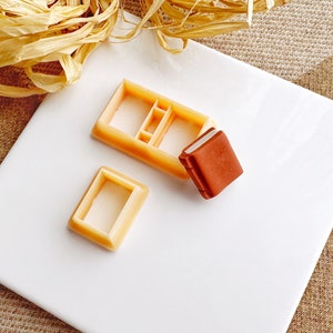 Può includere: Due stampi in plastica per realizzare forme di libri in pasta di zucchero o argilla polimerica. Uno stampo è aperto e l'altro è chiuso con un libro in pasta di zucchero marrone all'interno.