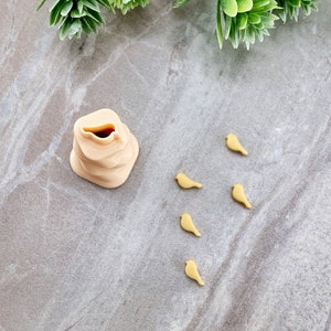 May include: A beige ceramic birdhouse with a small opening on the top. Six small, yellow, bird figurines are scattered around the birdhouse on a grey surface.