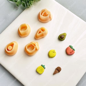 Può includere: Un set di nove stampi in silicone per la creazione di miniature alimentari. Gli stampi hanno la forma di una pesca, un avocado, un limone, un ananas, un cono gelato e alcune altre forme di frutta. Gli stampi sono realizzati in silicone trasparente e flessibile.
