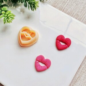 Pode incluir: Três cortadores de biscoitos em forma de coração, um é um coração simples e dois são lábios. Os cortadores de biscoitos estão sobre uma superfície branca.