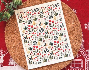 May include: A rectangular card with a botanical pattern of red berries, green leaves, and yellow accents. The card is on a round cork coaster, set against a red and white patterned background.