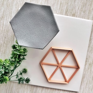 May include: Two hexagonal trays, one gray and one wood, on a white surface with a sprig of green foliage.