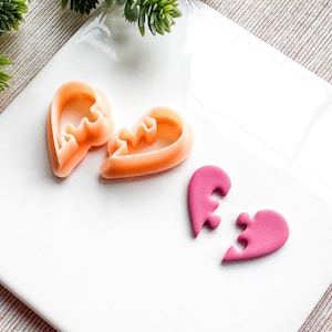 Pode incluir: Duas peças de quebra-cabeça em forma de coração cor de pêssego e duas peças de quebra-cabeça em forma de coração cor de rosa sobre uma superfície branca.