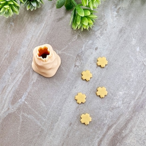 Może przedstawiać: Forma do pieczenia z jasnobrązowej ceramiki w kształcie ula z małym otworem na górze. Pięć małych, jasnobrązowych ciasteczek w kształcie gwiazd rozrzuconych wokół formy na jasnoszarym tle.