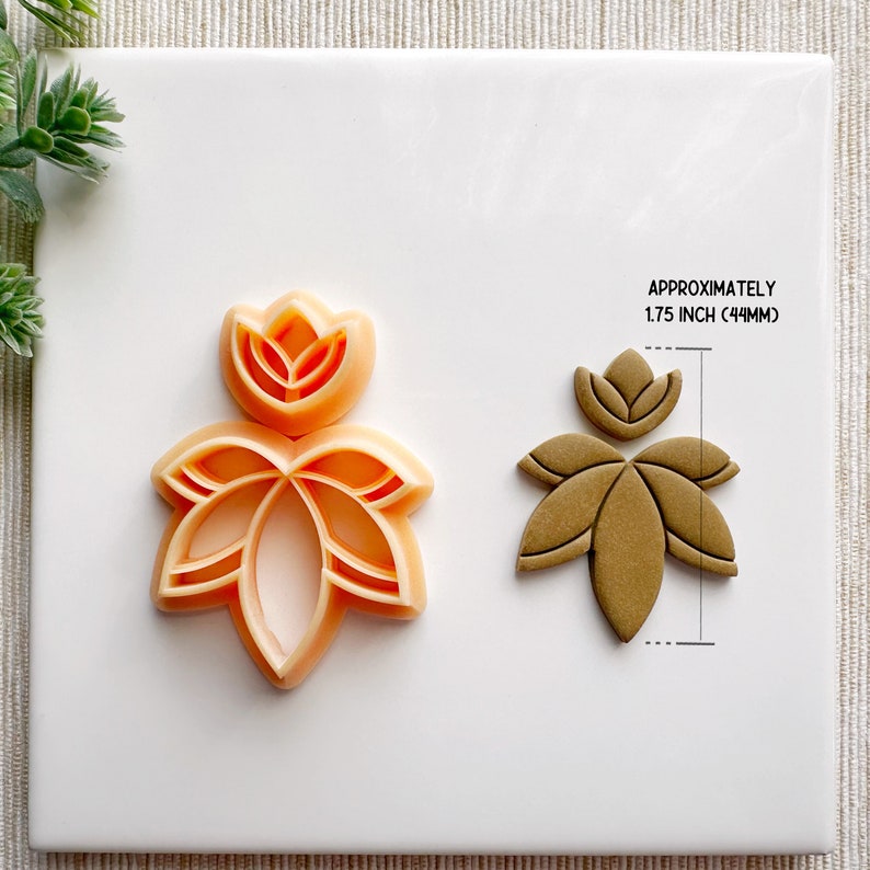 May include: A set of two cookie cutters in the shape of a stylized flower. The cutters are made of orange plastic and are approximately 1.75 inches (44 mm) in size.
