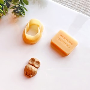 May include: Three cookie cutters on a white surface. The cutters are shaped like an owl, a ring, and a rectangle with the text "Babylon Cutters".