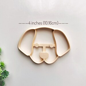 May include: A 4-inch (10.16 cm) cookie cutter in the shape of a dog's head. The cutter is made of beige plastic.