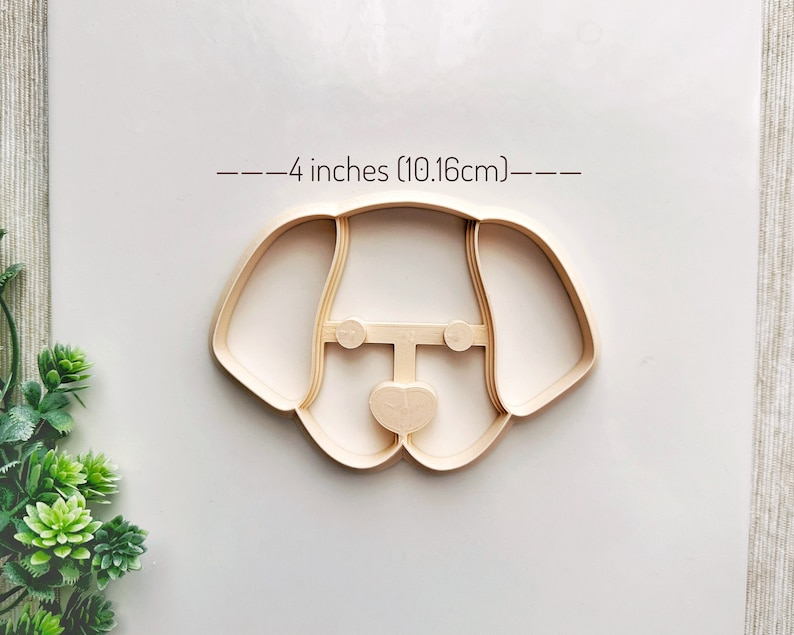 May include: A 4-inch (10.16 cm) cookie cutter in the shape of a dog's head. The cutter is made of beige plastic.