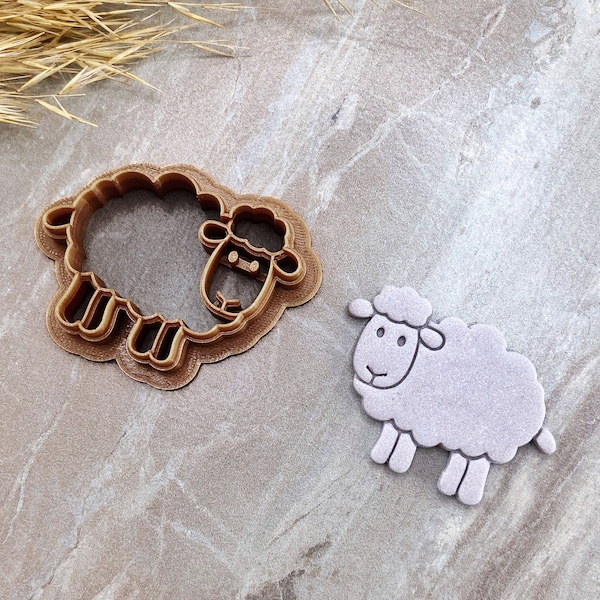 May include: A brown plastic cookie cutter shaped like a sheep, next to a white felt sheep cutout.
