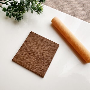 May include: A brown leather square and a light orange foam roller on a white surface.