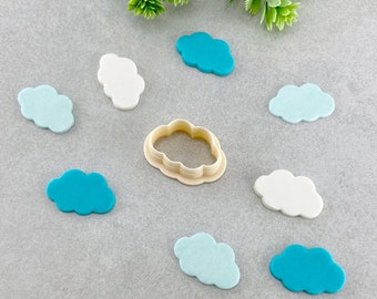 Puede incluir: Un conjunto de ocho cortadores de galletas en forma de nube de diferentes colores, incluyendo azul, azul claro y blanco. Los cortadores están dispuestos sobre una superficie gris. Uno de los cortadores es un molde de plástico.
