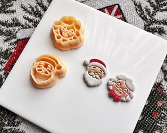 May include: Three Christmas-themed cookie cutters, one shaped like a Santa Claus, one shaped like a woman with a white hat, and one shaped like a wreath. The cutters are made of a light beige plastic.
