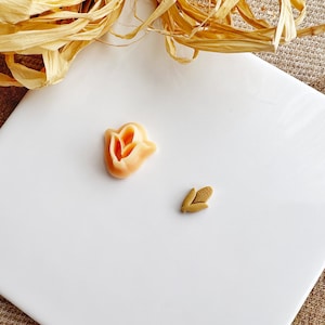 Peut inclure: Deux petites formes de fleurs en argile, une orange et une brune, sur un fond blanc.