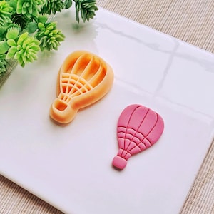 May include: Two hot air balloon cookie cutters, one is orange and the other is pink.