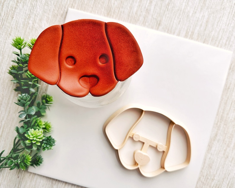 May include: A brown dog-shaped cookie cutter and a red dog-shaped cookie cutter on a white surface.