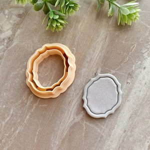 May include: Two cookie cutters, one with a scalloped edge and one with a smooth edge, both in a light brown color.