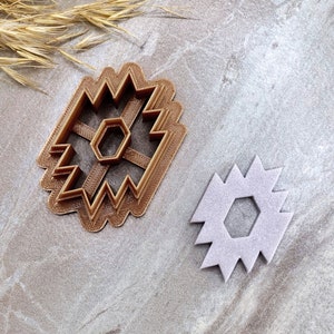 May include: Two brown plastic cookie cutters in the shape of a geometric star with a hexagonal center hole. The cutters are on a light gray textured surface.