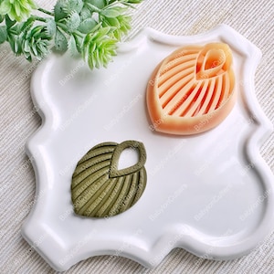 Peut inclure: Deux moules en silicone pour la création. Un moule est de couleur pêche et en forme de feuille avec un design détaillé. L'autre moule est vert et en forme de feuille avec un design détaillé.